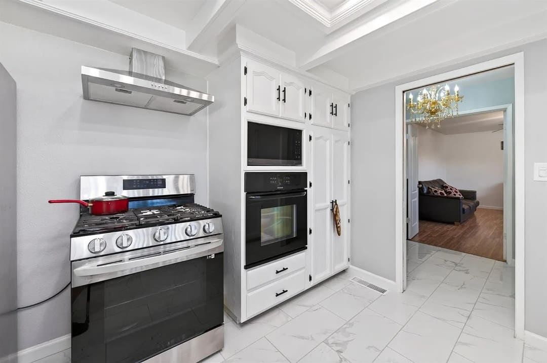 A kitchen with a stainless steel gas range and matching hood on the left, and tall white built-in cabinetry with a microwave and oven in the center.