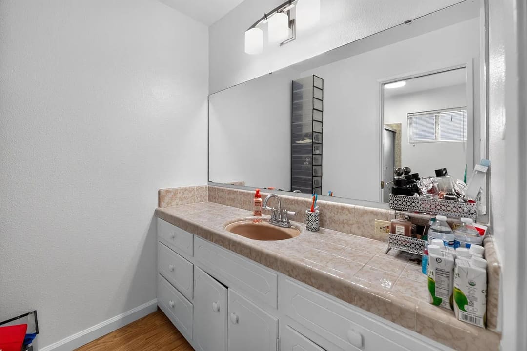 A bathroom vanity area with a long marble-look countertop, a single sink, and a large wall mirror above it.