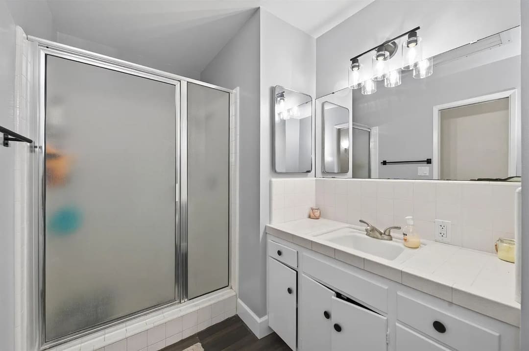 A bathroom is shown with a frosted glass shower enclosure on the left and a white vanity with a sink on the right.