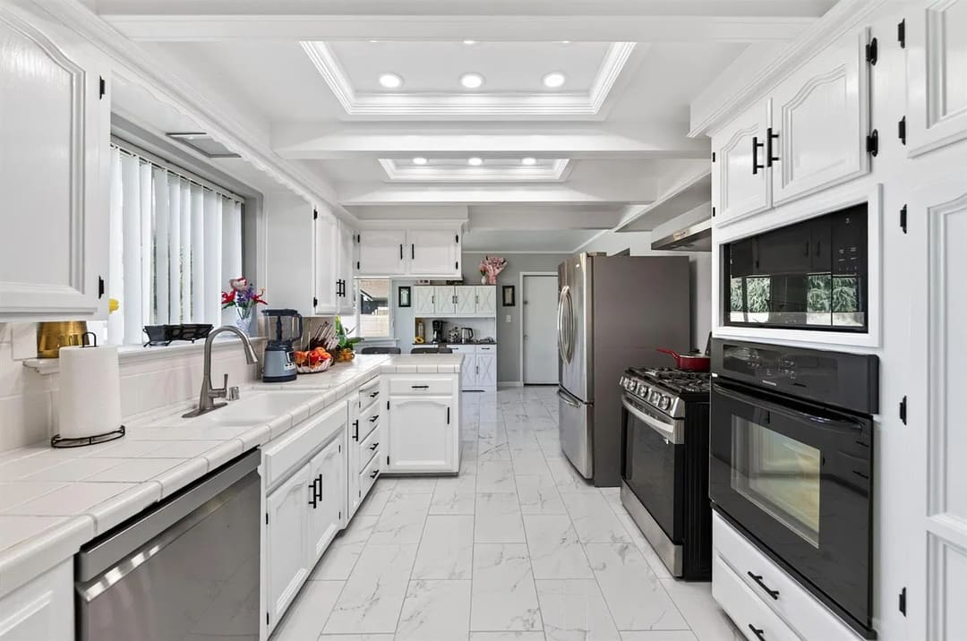 A bright white galley kitchen with cabinets and appliances on both sides and a small sink area under a window on the left.